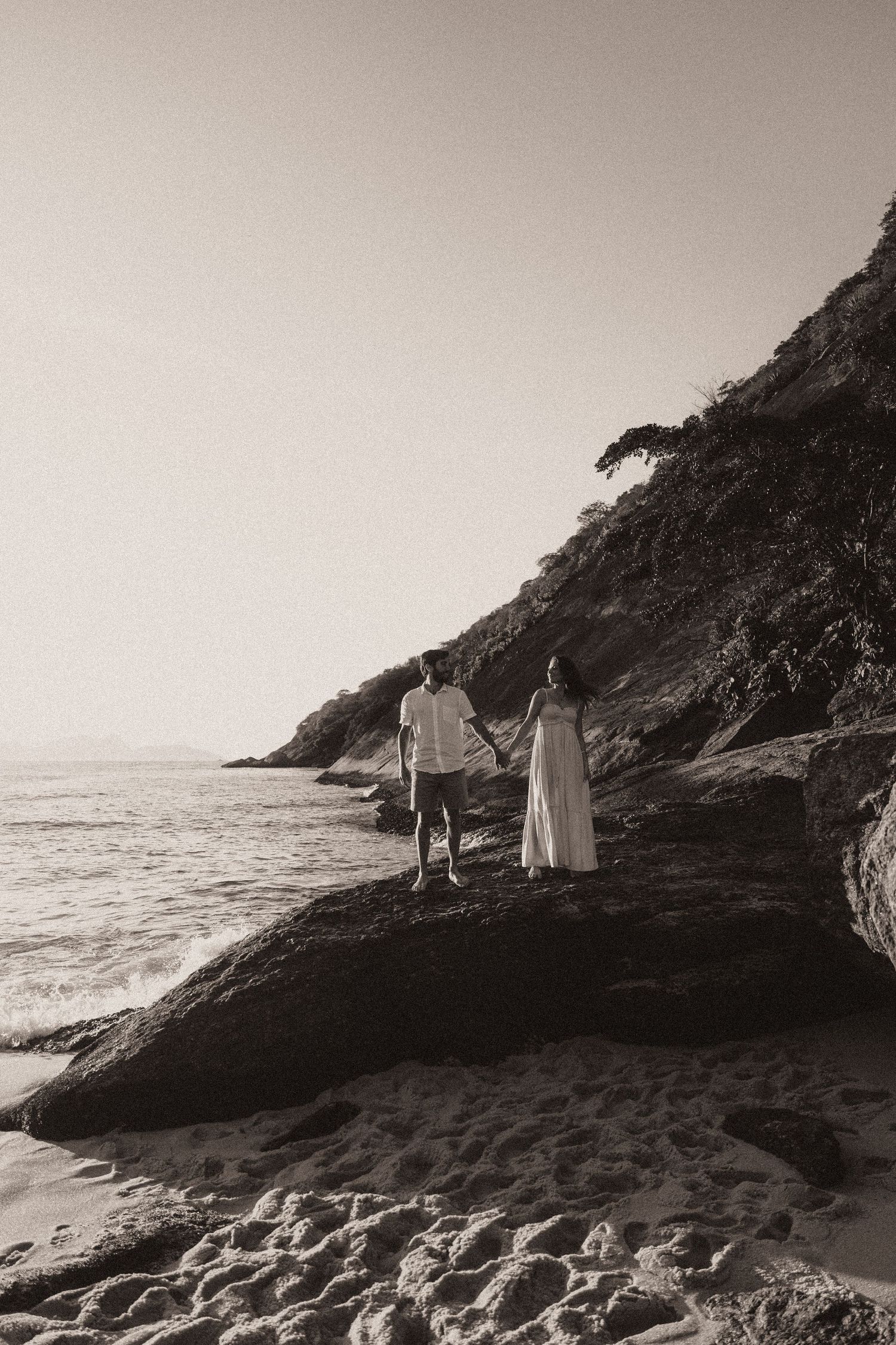 Romantic black and white panoramic series showing people walking along rocky coastal cliffs at sunset by the ocean.