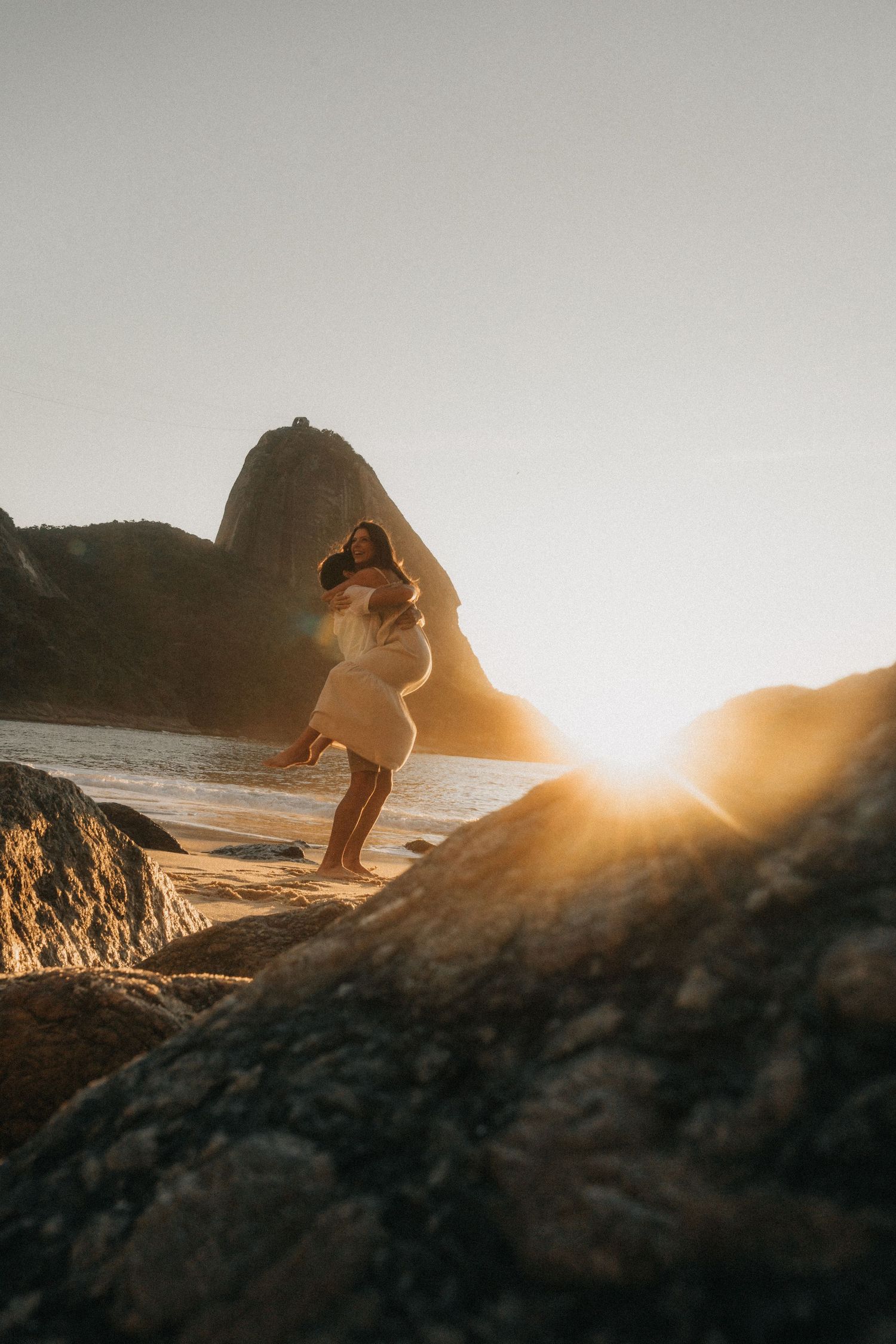 Silhouettes of figures stand near ocean cliffs at sunset creating romantic golden hour atmosphere.