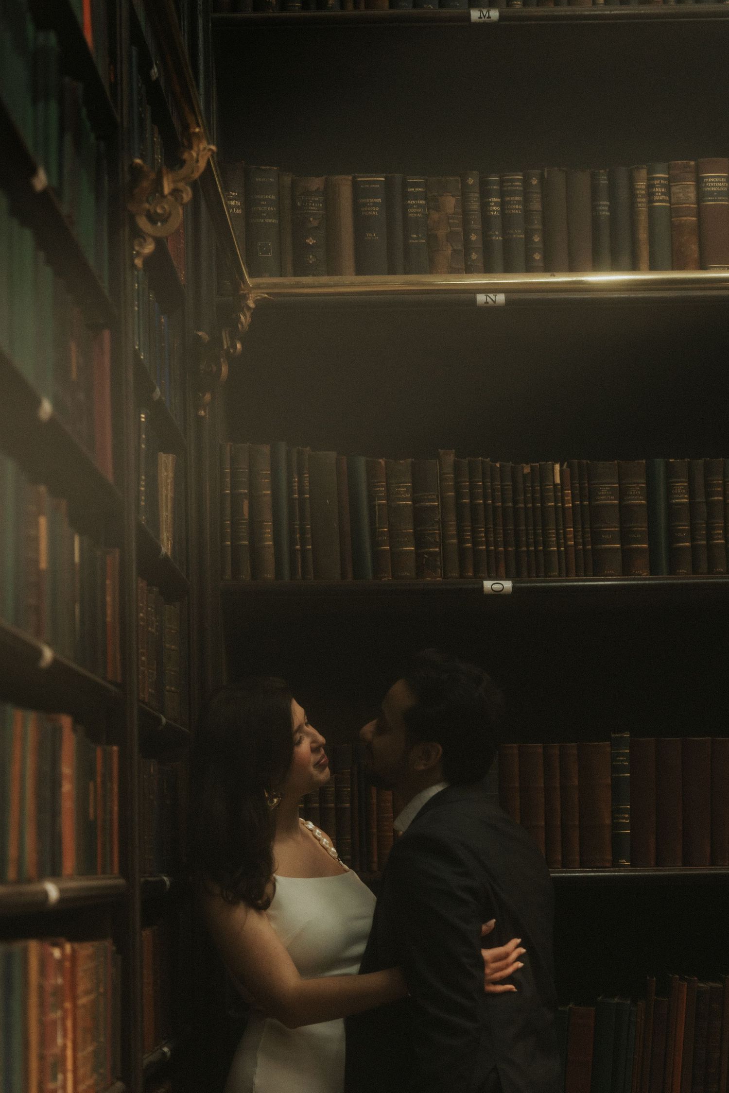 Moody scene in a dark library with bookshelves lining the walls and someone reading in dim lighting.