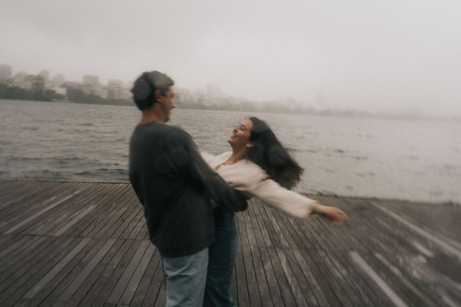 Young couple embraces while standing on a wooden boardwalk by the ocean at dusk.