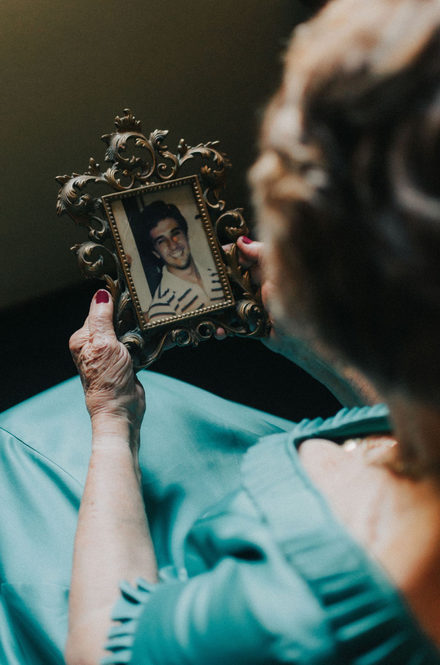 Hands in blue medical gloves hold a small ornate picture frame against a dark background.