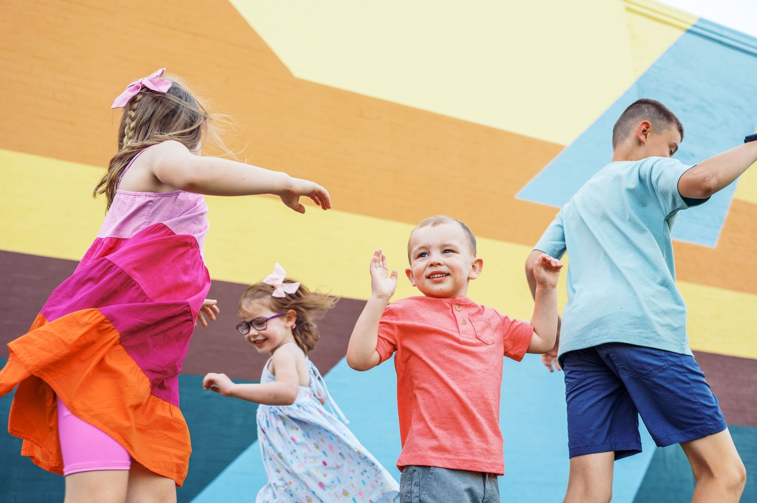 Children in colorful clothing playing against vibrant orange and blue wall.