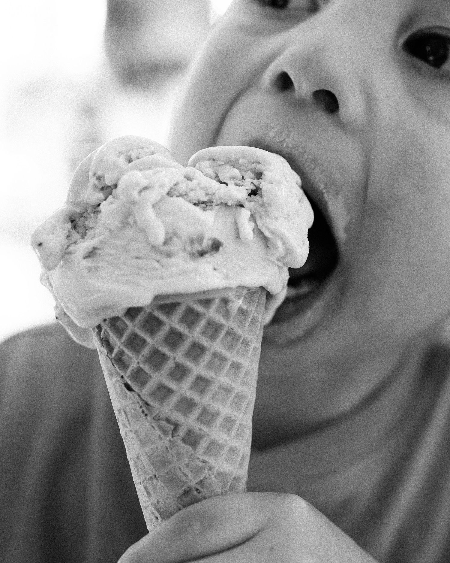 Close-up black and white photo of someone taking a big bite of ice cream cone.