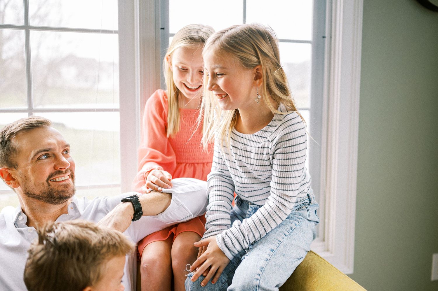 A happy family shares joyful moments together on a yellow couch by a bright window.