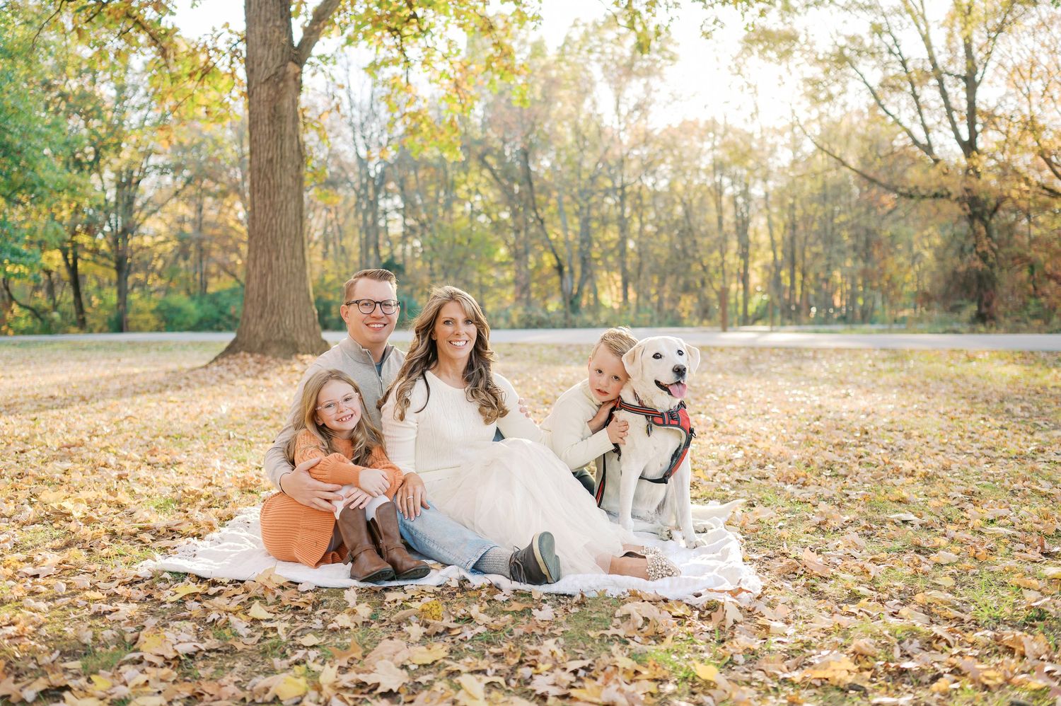 A playful autumn photoshoot in a park with warm golden sunlight filtering through trees and fallen leaves.