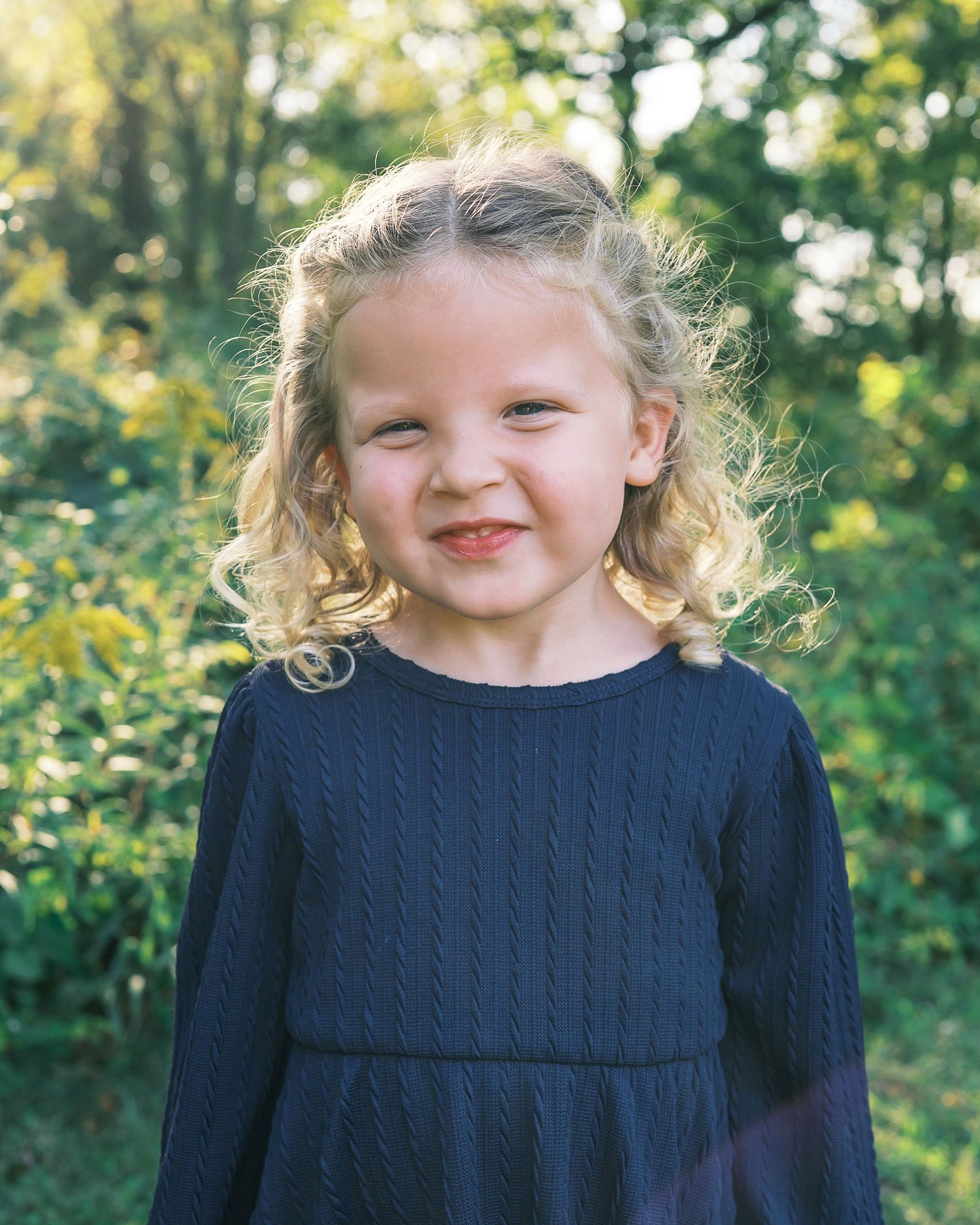 A close-up portrait shot in a navy blue sweater against a green natural background.