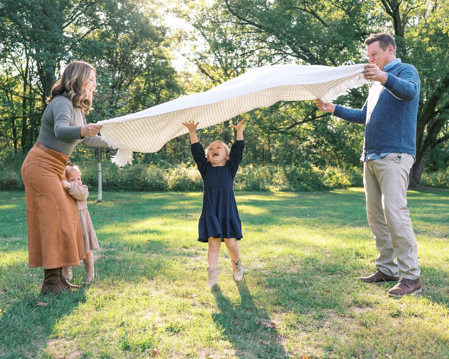 A joyful outdoor scene with a white blanket being playfully waved in a sunlit garden setting.