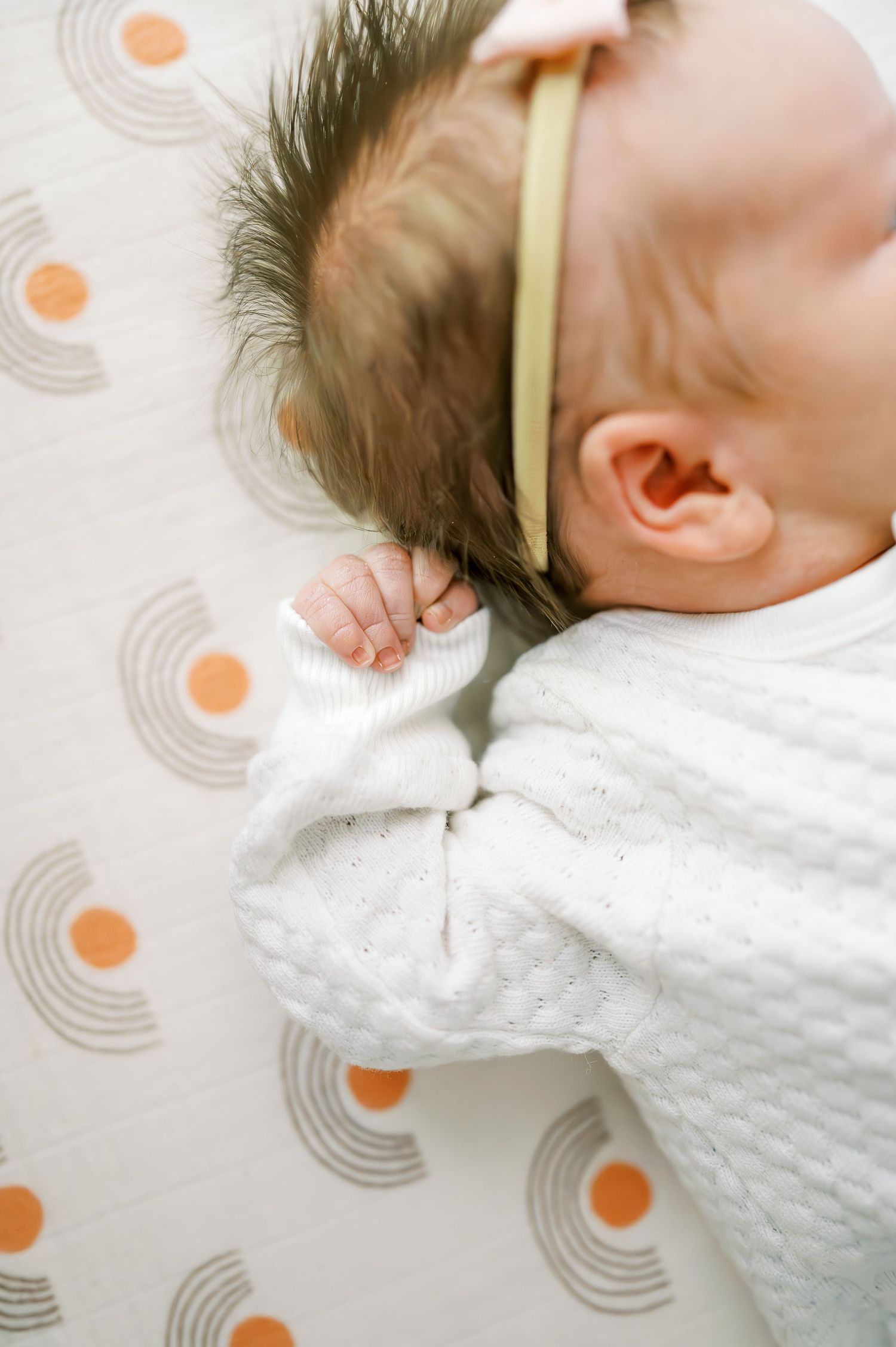 Close-up of sleeping infant in white outfit against geometric patterned background.