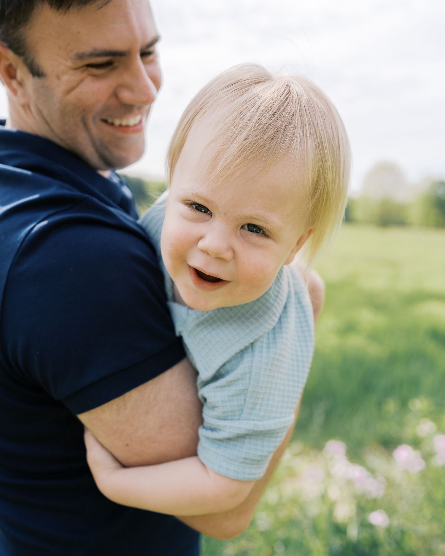 A sweet candid moment between parent and child laughing together in a meadow.