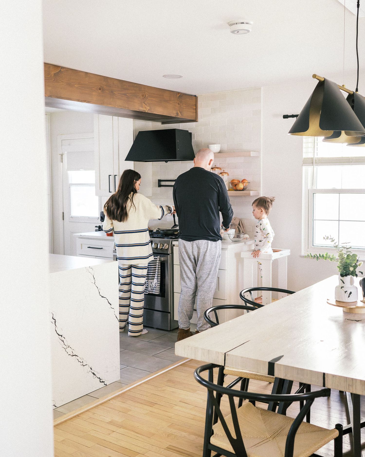 Family cooking together in a bright, modern kitchen with wood beam and black pendant lights.
