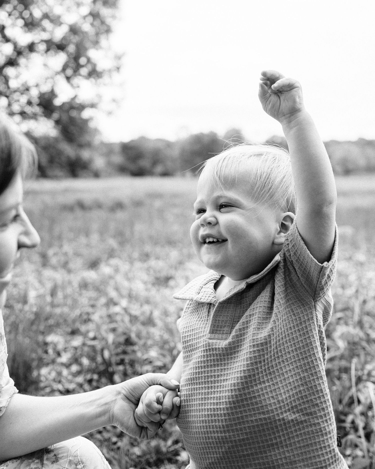 Black and white candid photo of a toddler laughing and playing in a field.