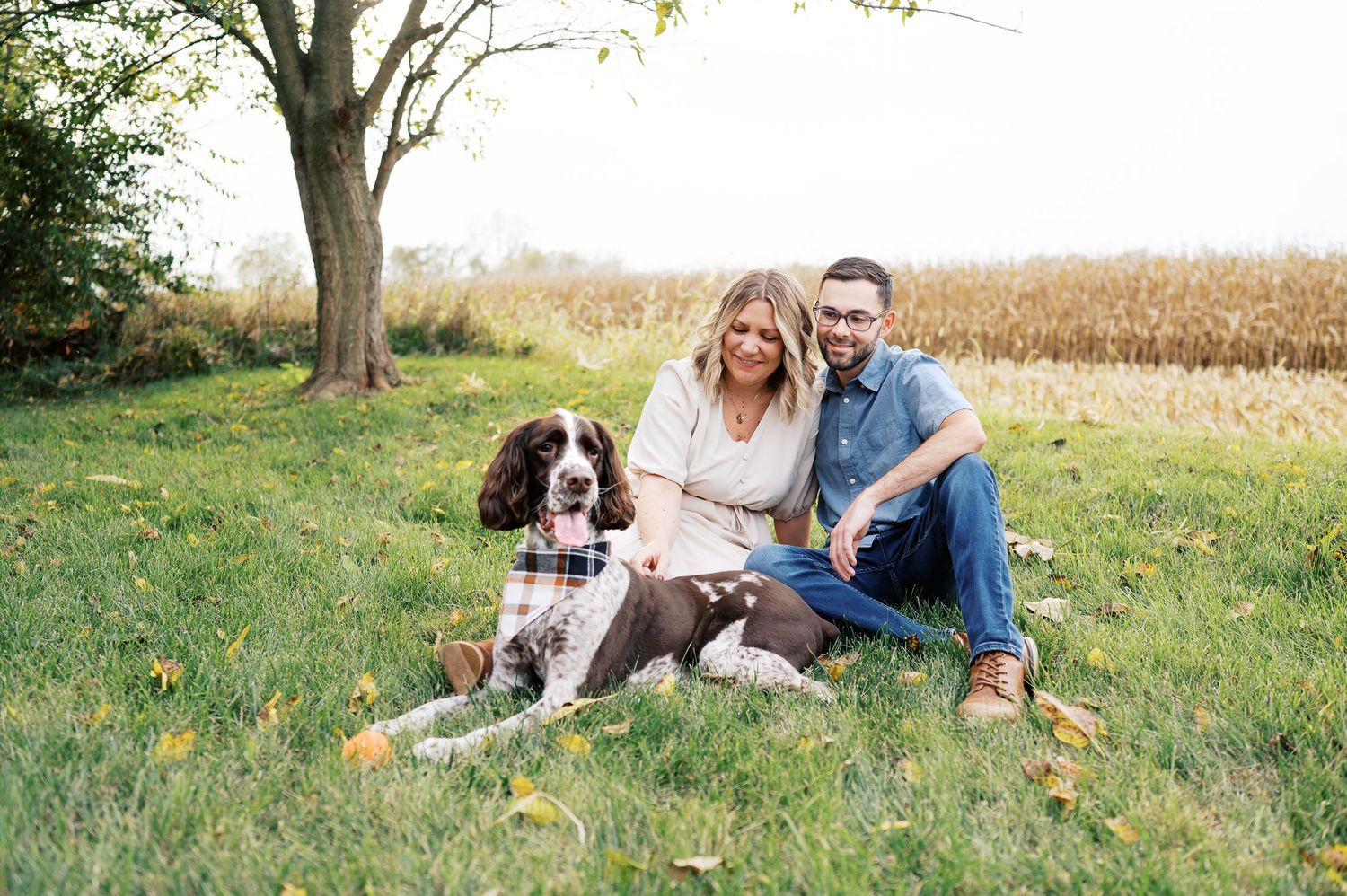 Couple sitting together on grass with their dog during an autumn outdoor photoshoot.