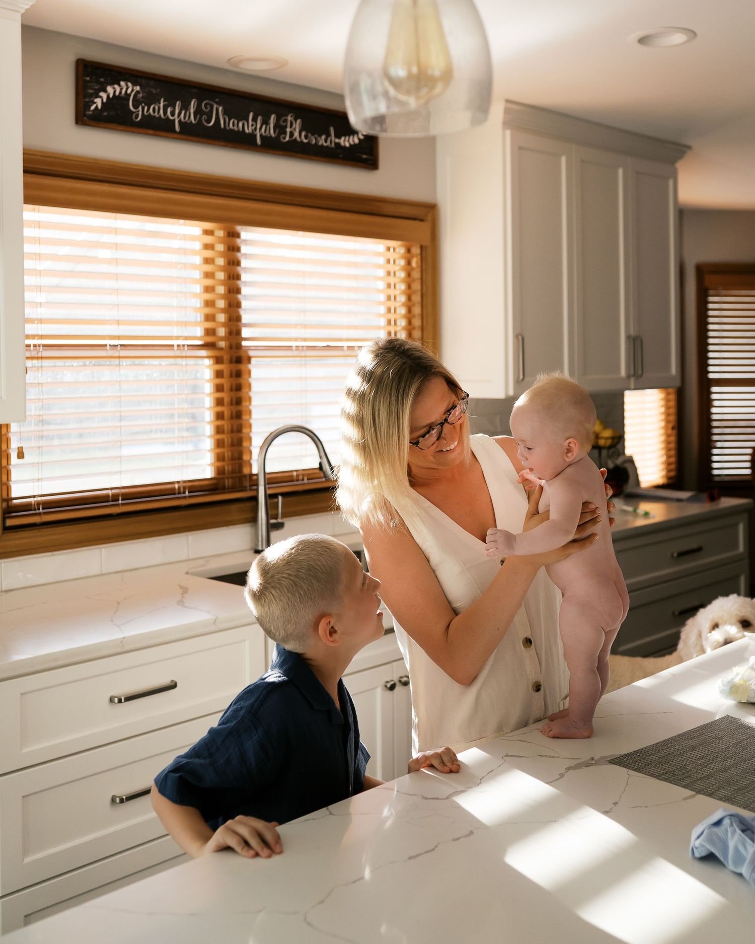 Sweet playtime moment in bright kitchen as caregiver interacts with baby at sink.