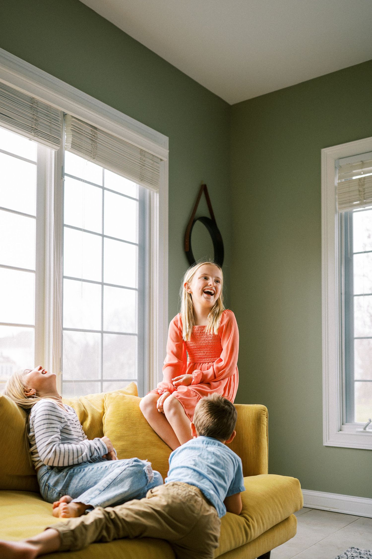 Candid moments of laughter and play between family members on a yellow couch.