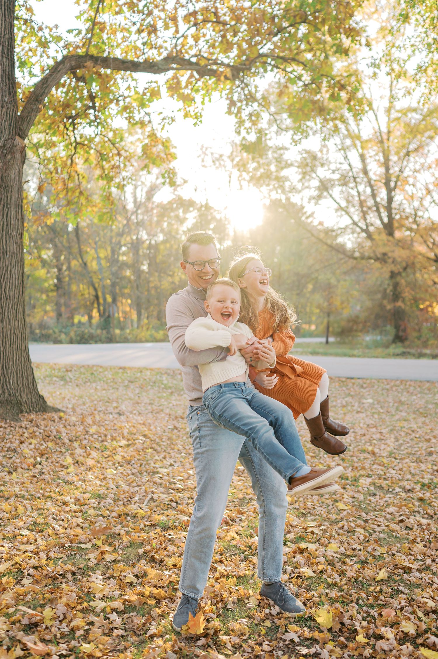 Family playing and laughing together in park surrounded by fall foliage.