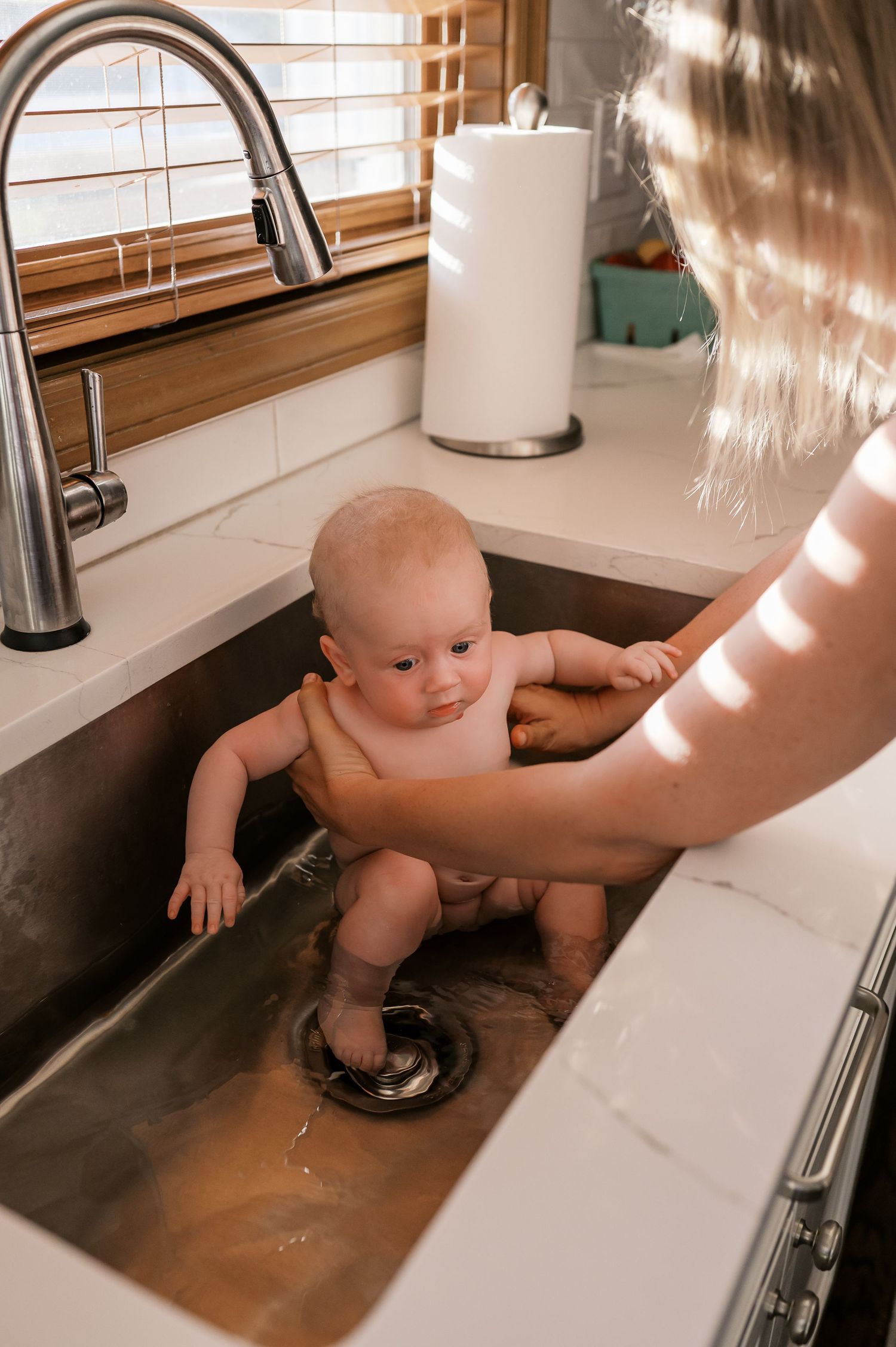 Curious baby exploring stainless steel kitchen sink during bath time.