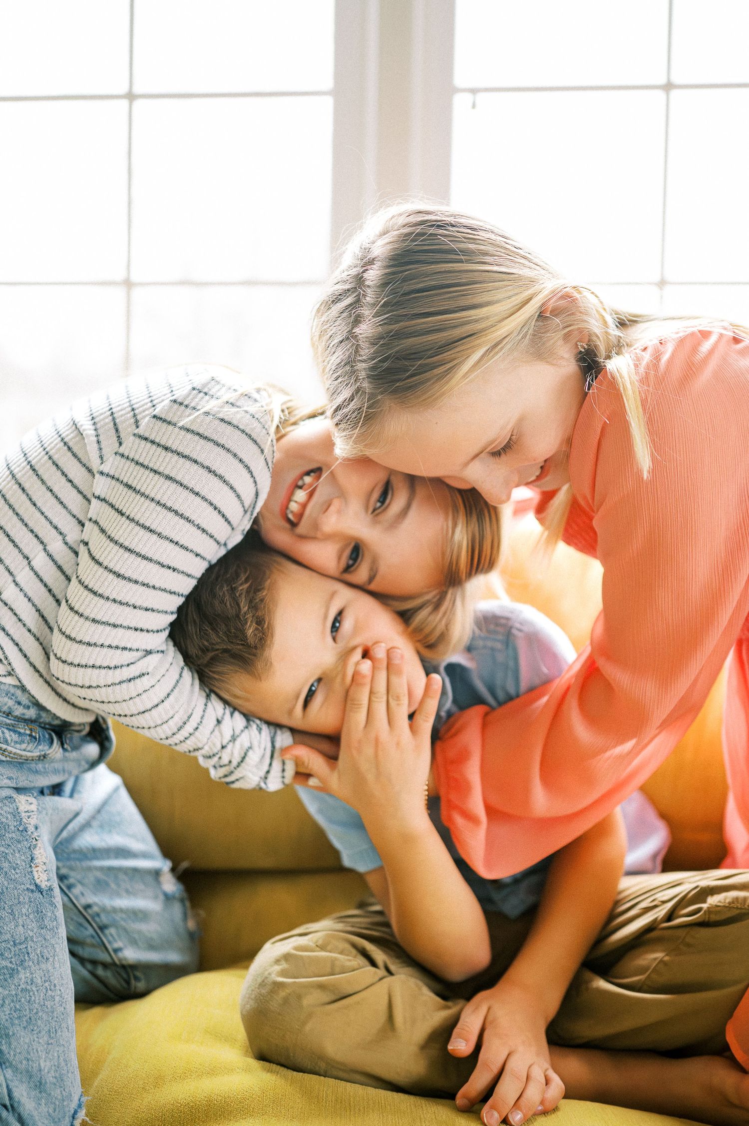Two people share an intimate moment while laying on a yellow couch in natural sunlight.