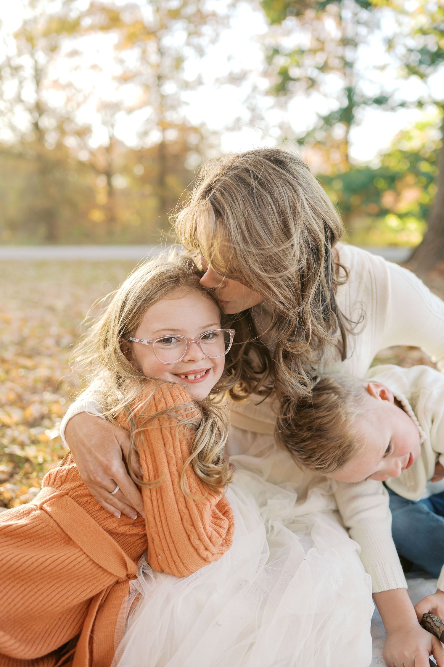 Family sharing tender moment while sitting on ground covered in fall leaves.