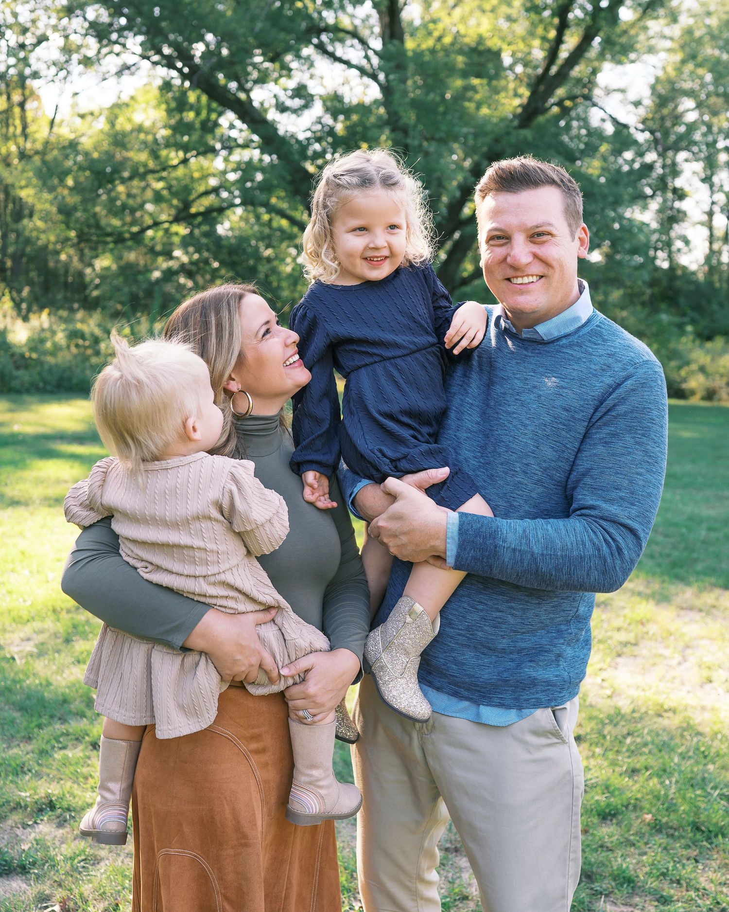 Family shares joyful candid moments together in an outdoor autumn setting wearing coordinated blue and beige outfits.