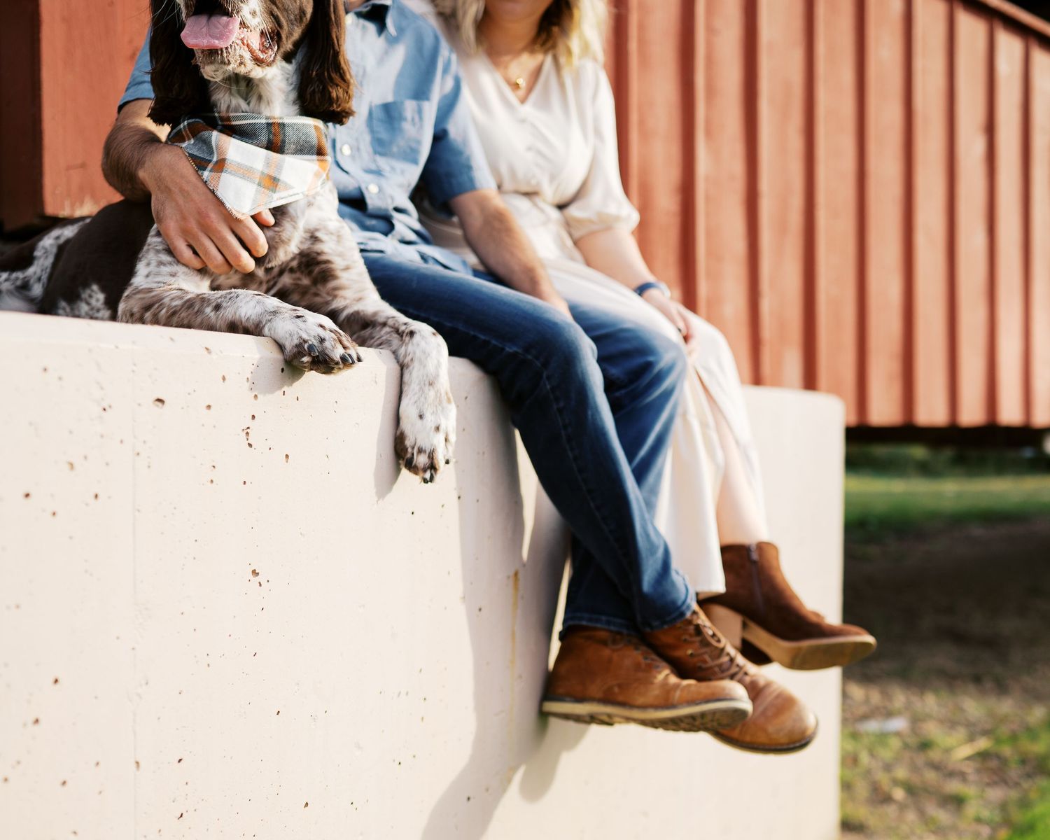 People sitting casually on a white concrete wall wearing jeans and boots on a sunny day.