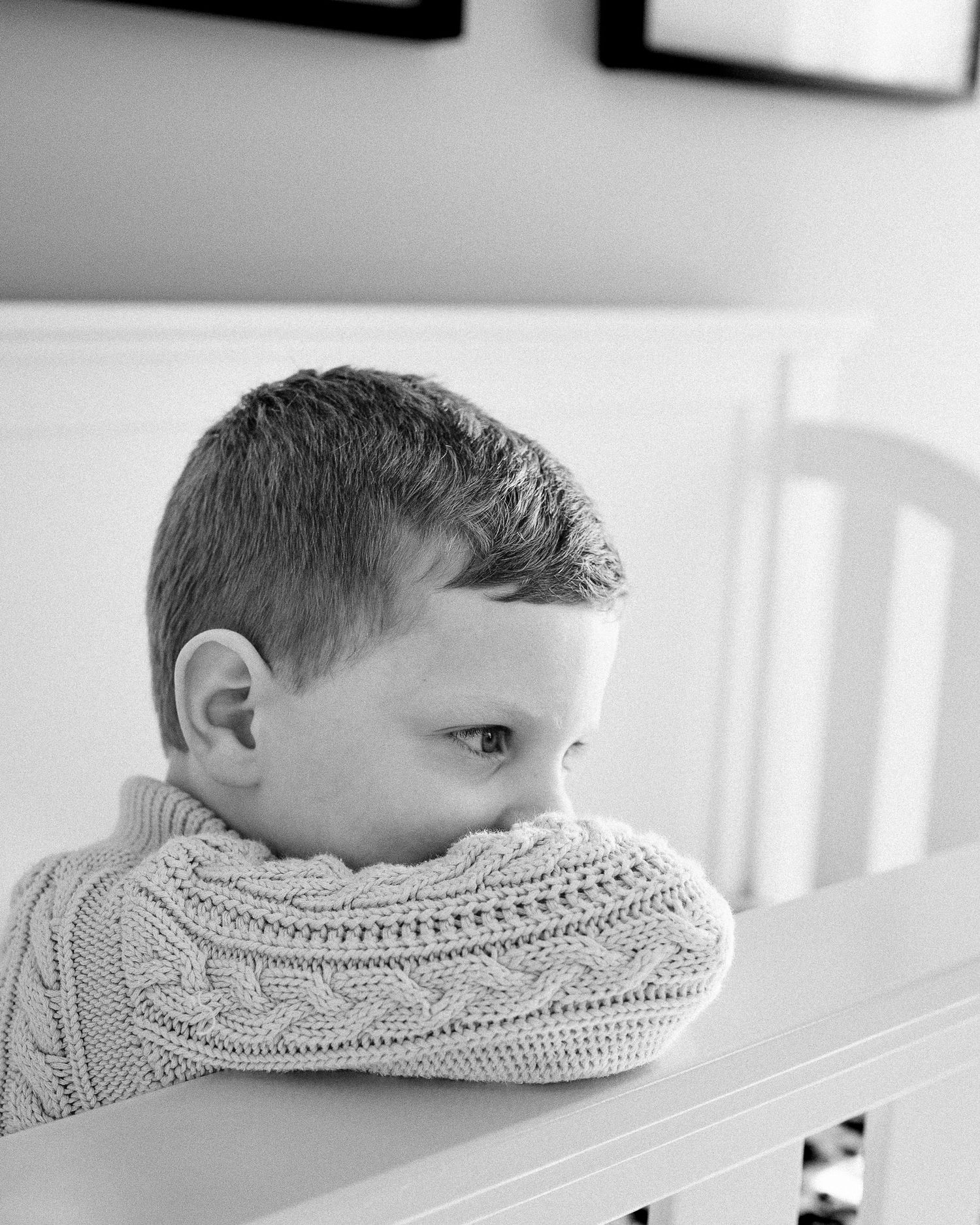 Black and white portrait of child peeking over cable knit sweater.