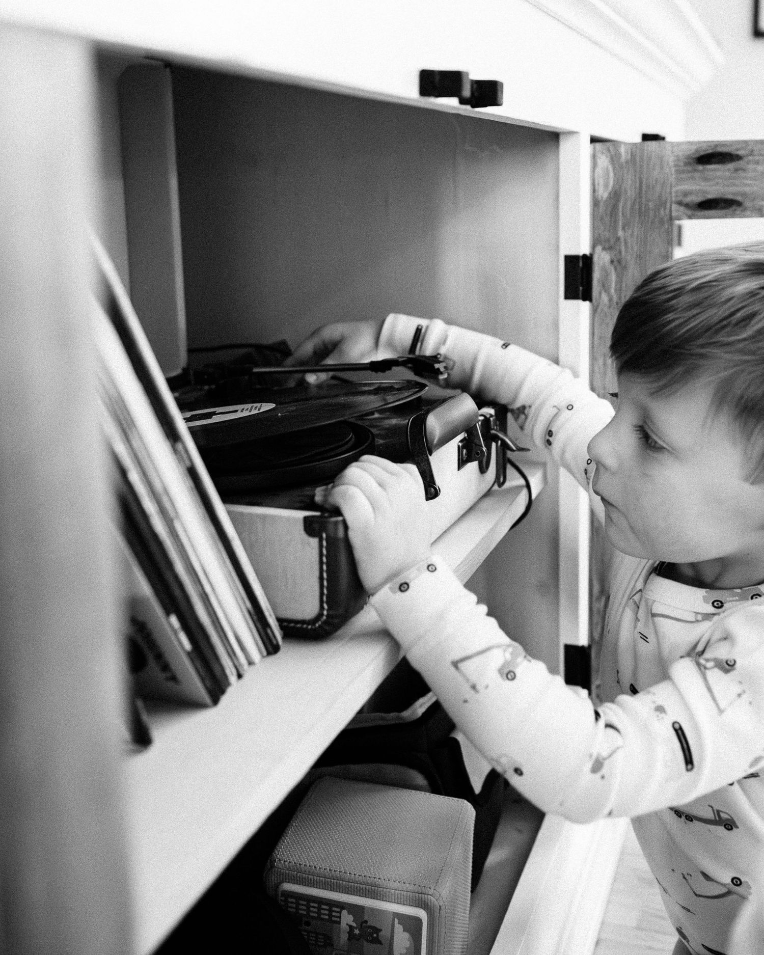 Small hands explore a wooden shelf filled with books and media in black and white.