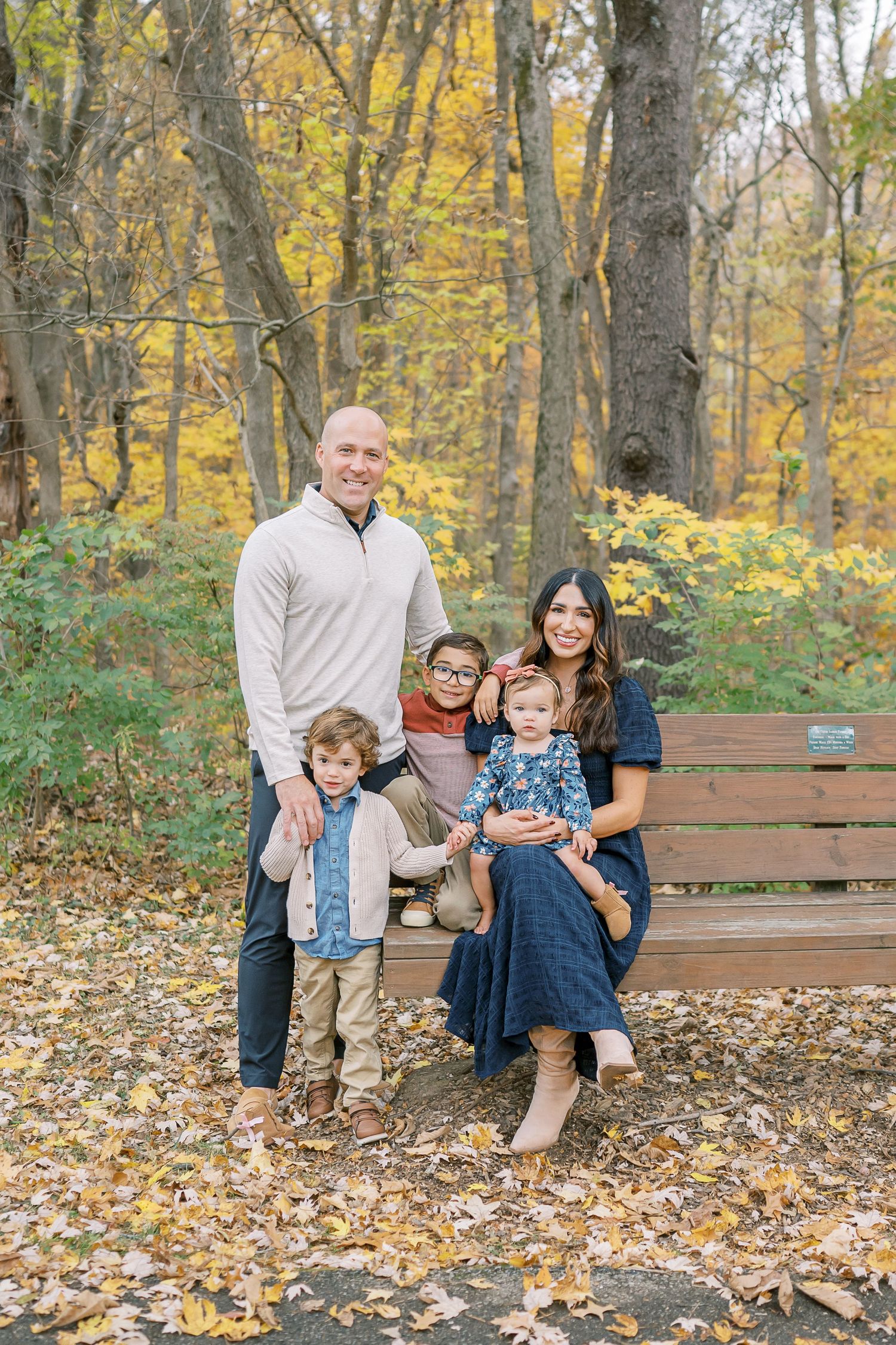 Family sitting together on wooden bench surrounded by fall foliage.