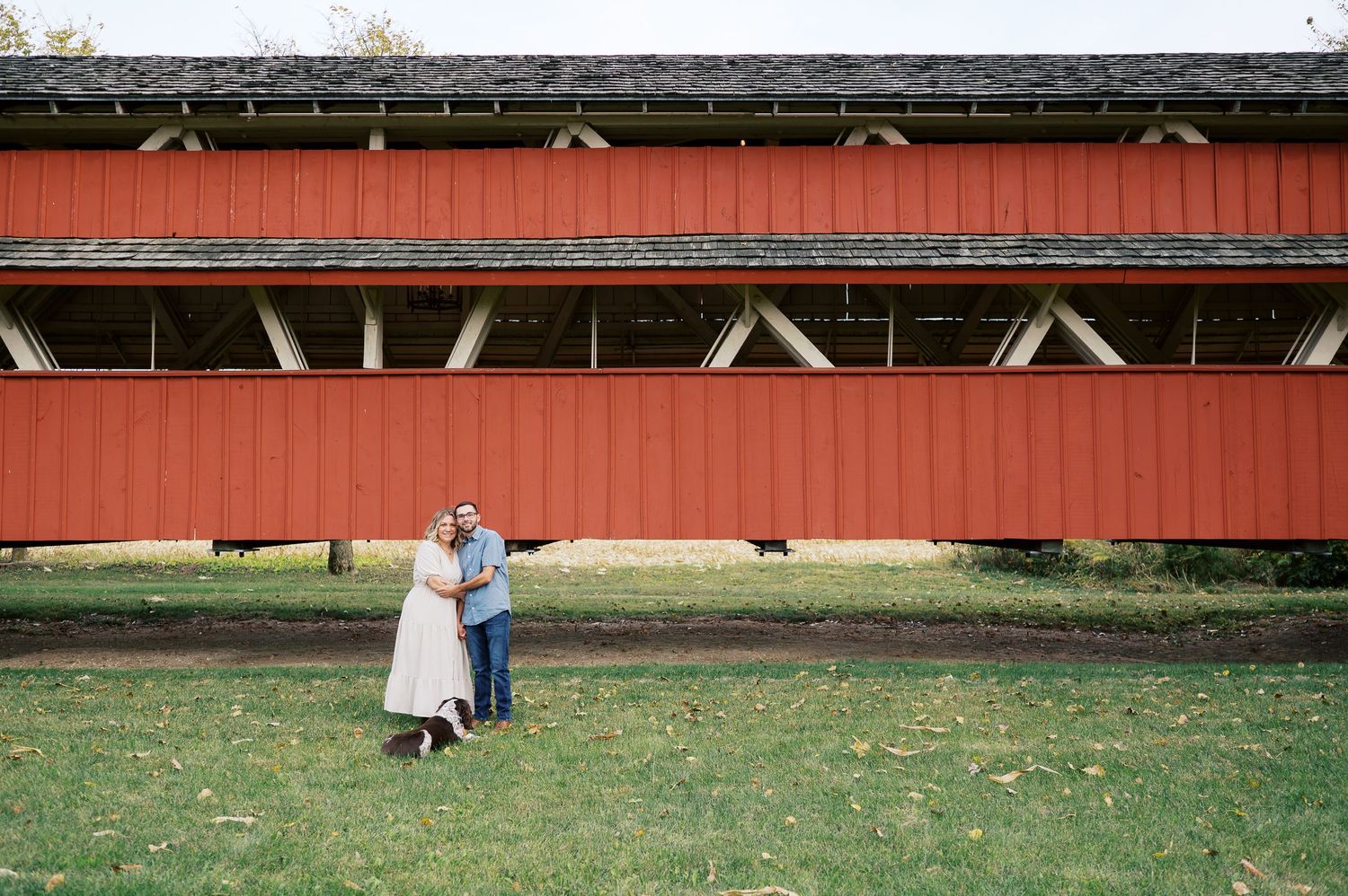 A series of connected red barn buildings with white trim stand against a green grassy field.
