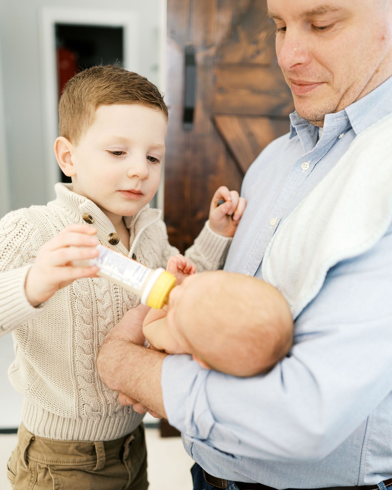 Family members gathering around to feed a baby with a bottle.