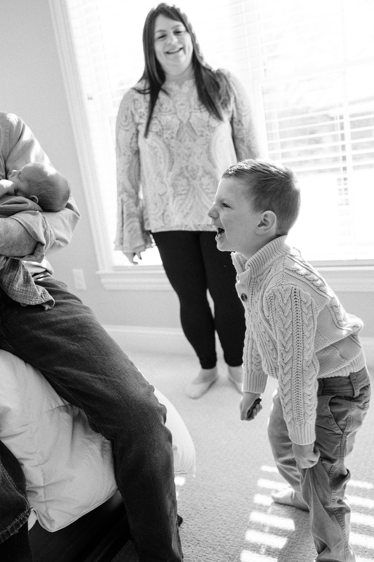 A black and white photo capturing a playful family moment in a sunlit room.