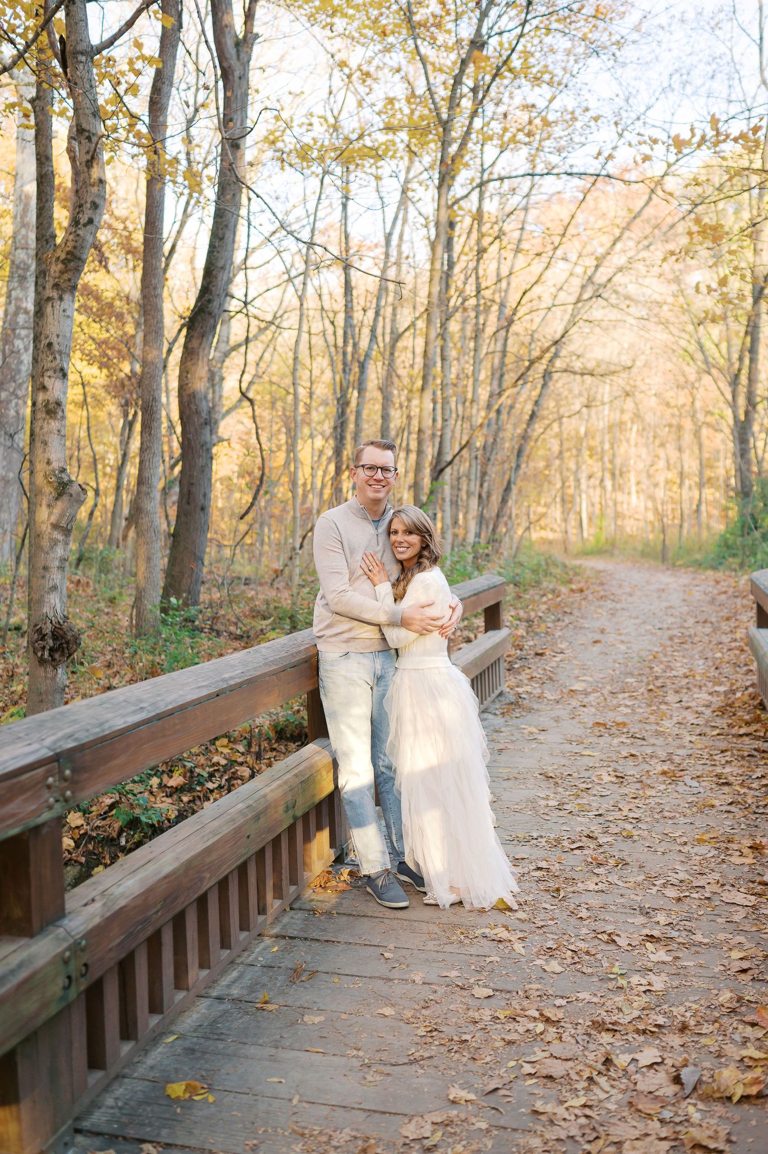 Couple embracing on wooden boardwalk surrounded by autumn trees.