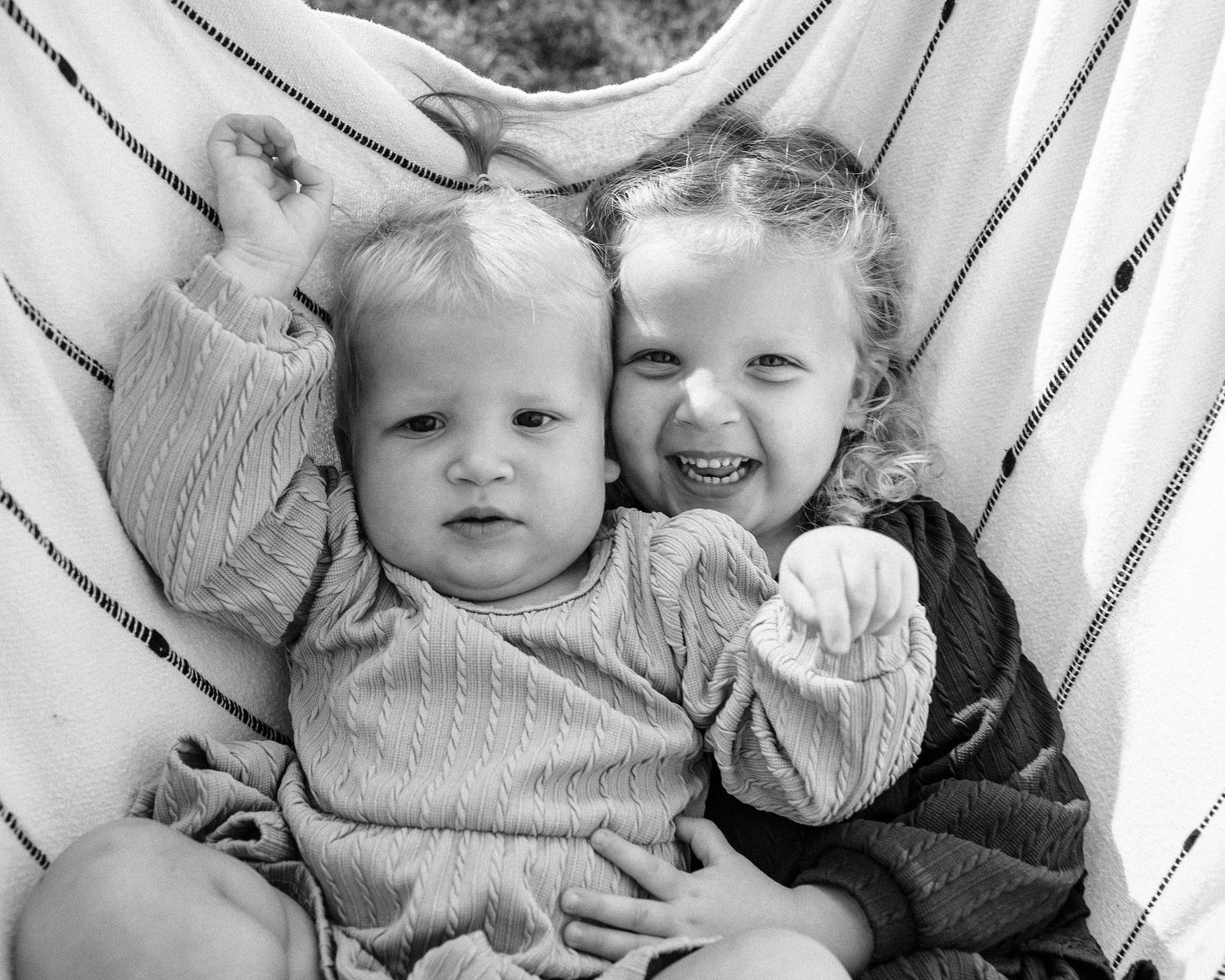 A black and white vintage photograph shows several children huddled together smiling in a casual group portrait.