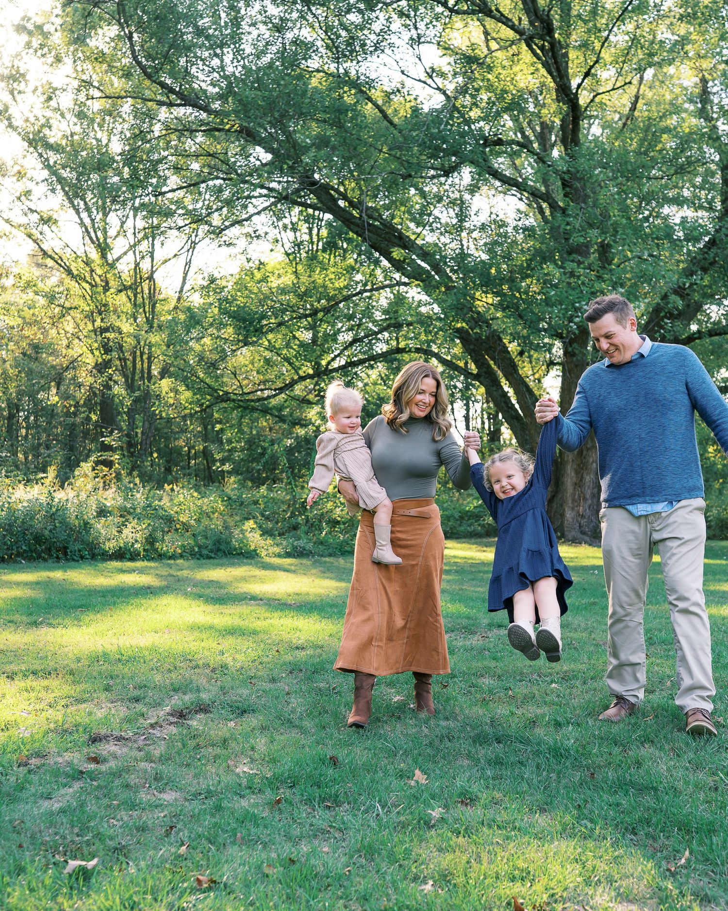 A playful sequence of people swinging and spinning a small child in a grassy outdoor setting.