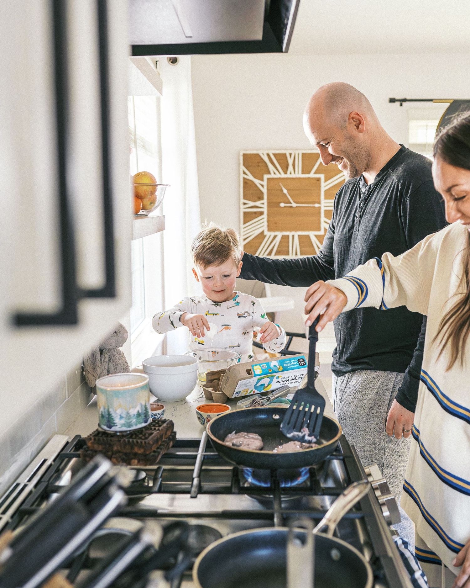 Family members gathered around a stove cooking together in a contemporary white kitchen.