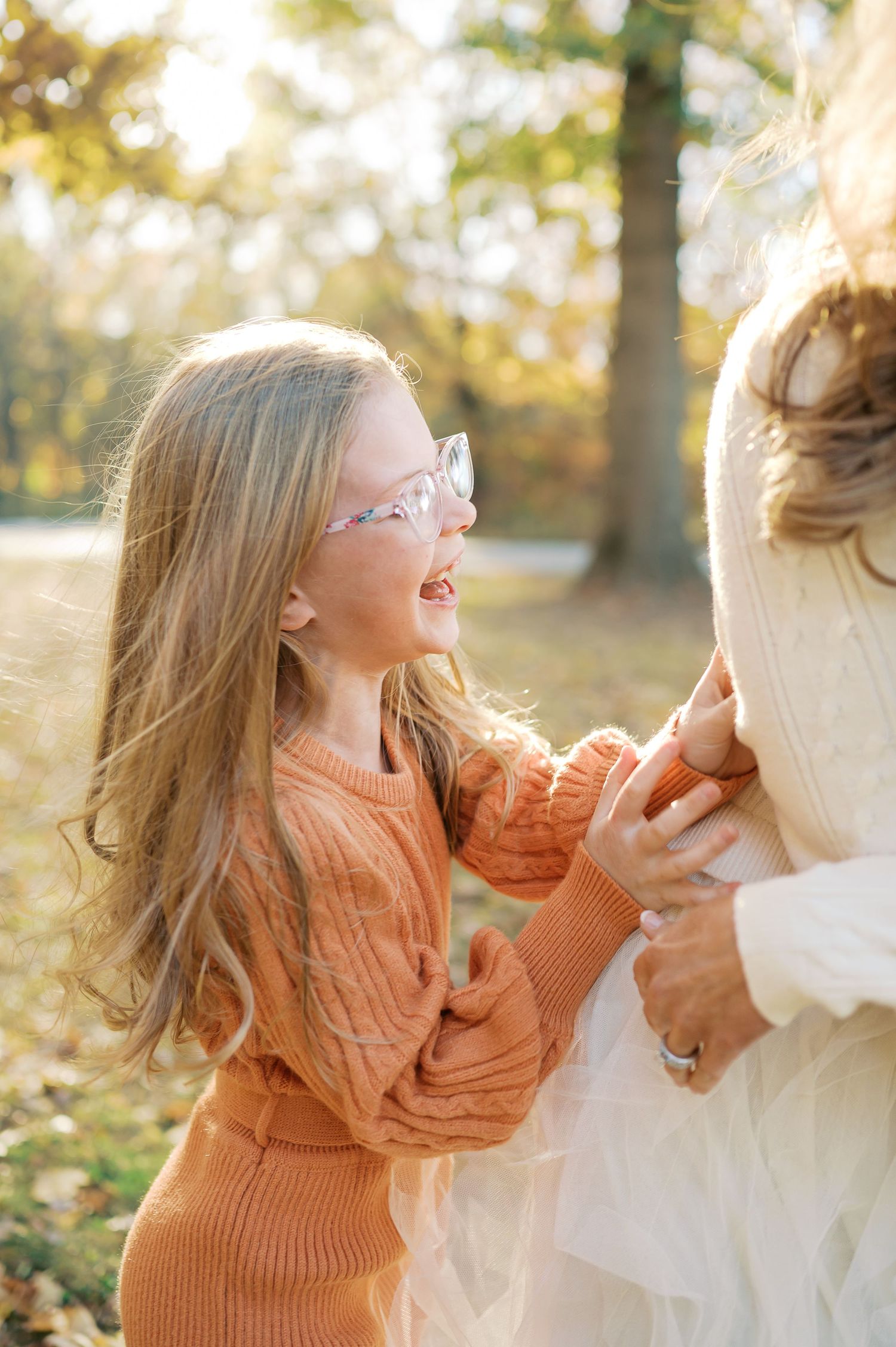 Family members laughing and playing together in an autumn park with golden sunlight filtering through trees.
