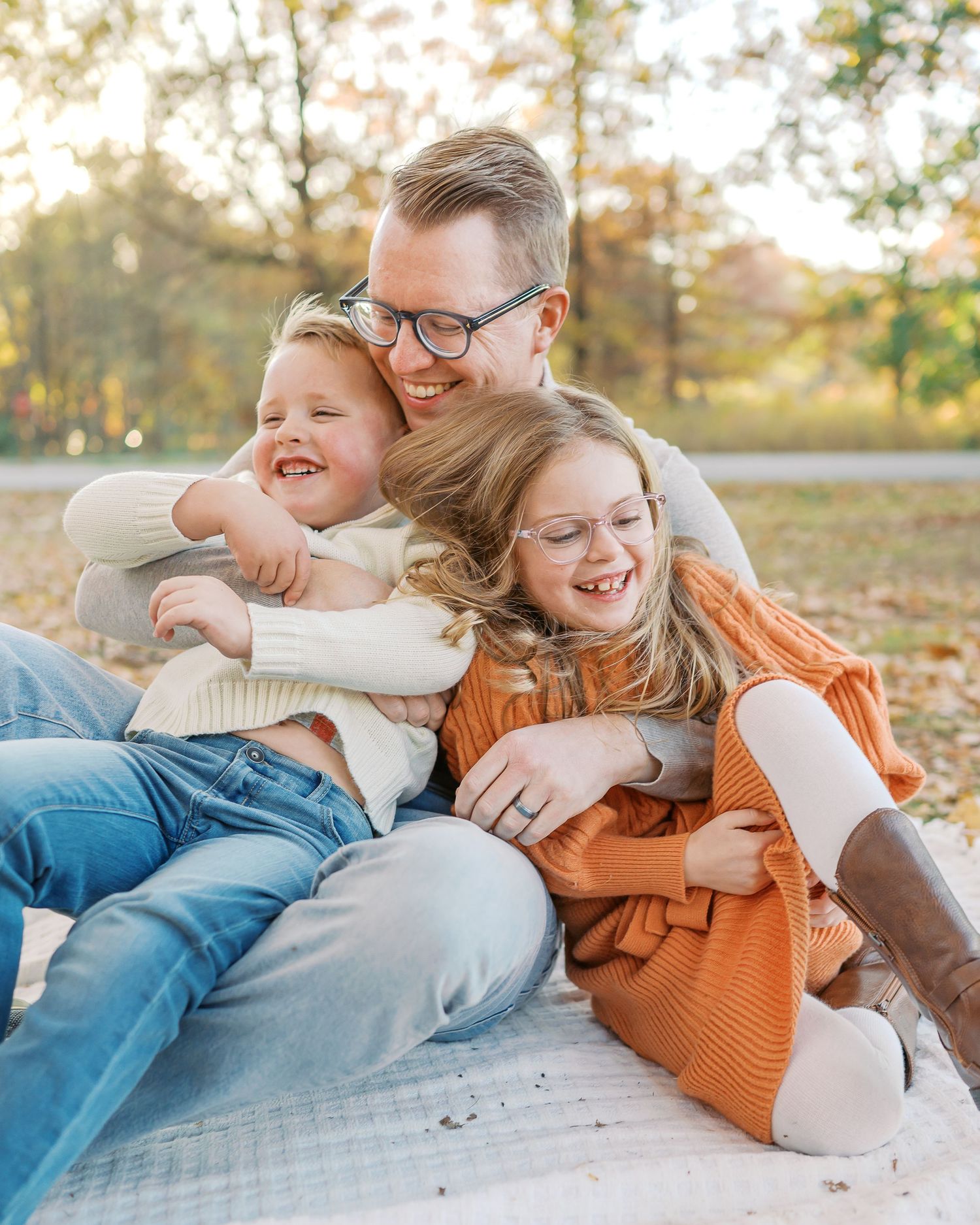 Family sharing joyful moment while sitting on blanket in autumn park.