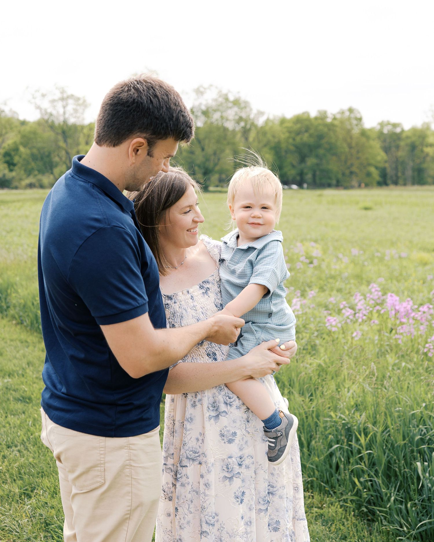 Family portrait session in a sunny meadow with wildflowers and natural lighting.
