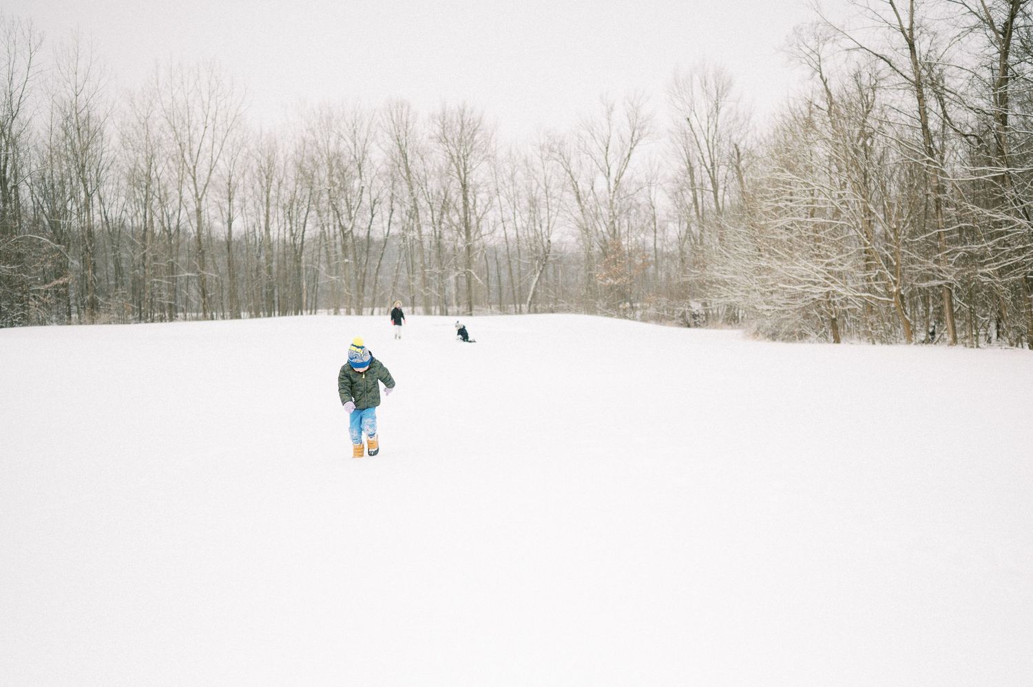 Children playing in snowy winter landscape with winter gear and hats.