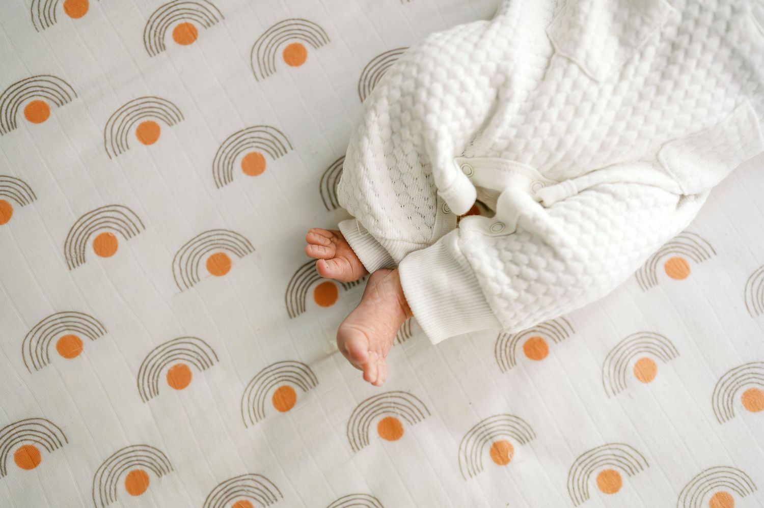 Baby in white knit sweater lying on patterned sheet with orange circular designs.