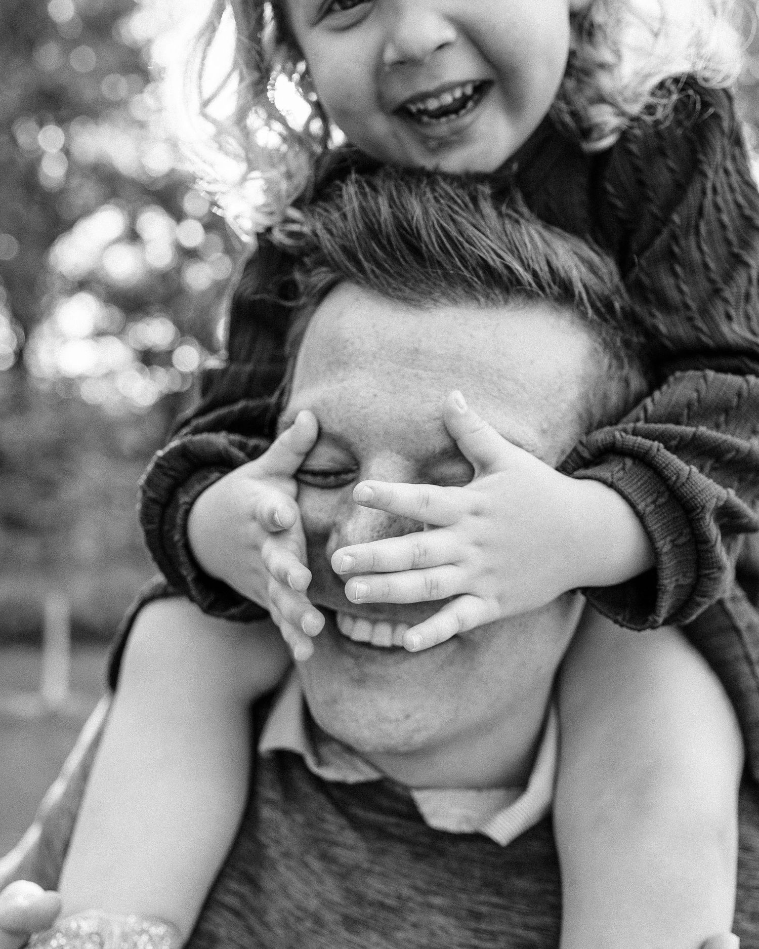 A playful black and white portrait capturing laughter and hands covering eyes.