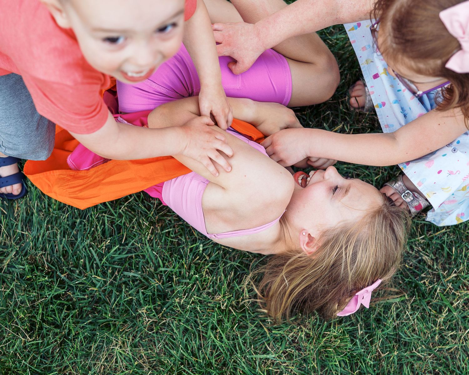 Children sprawled joyfully on green grass during a fun summer activity.