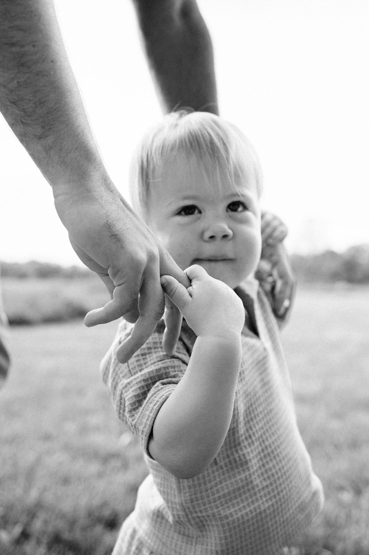 Black and white photo of small child holding adult's hand outdoors.
