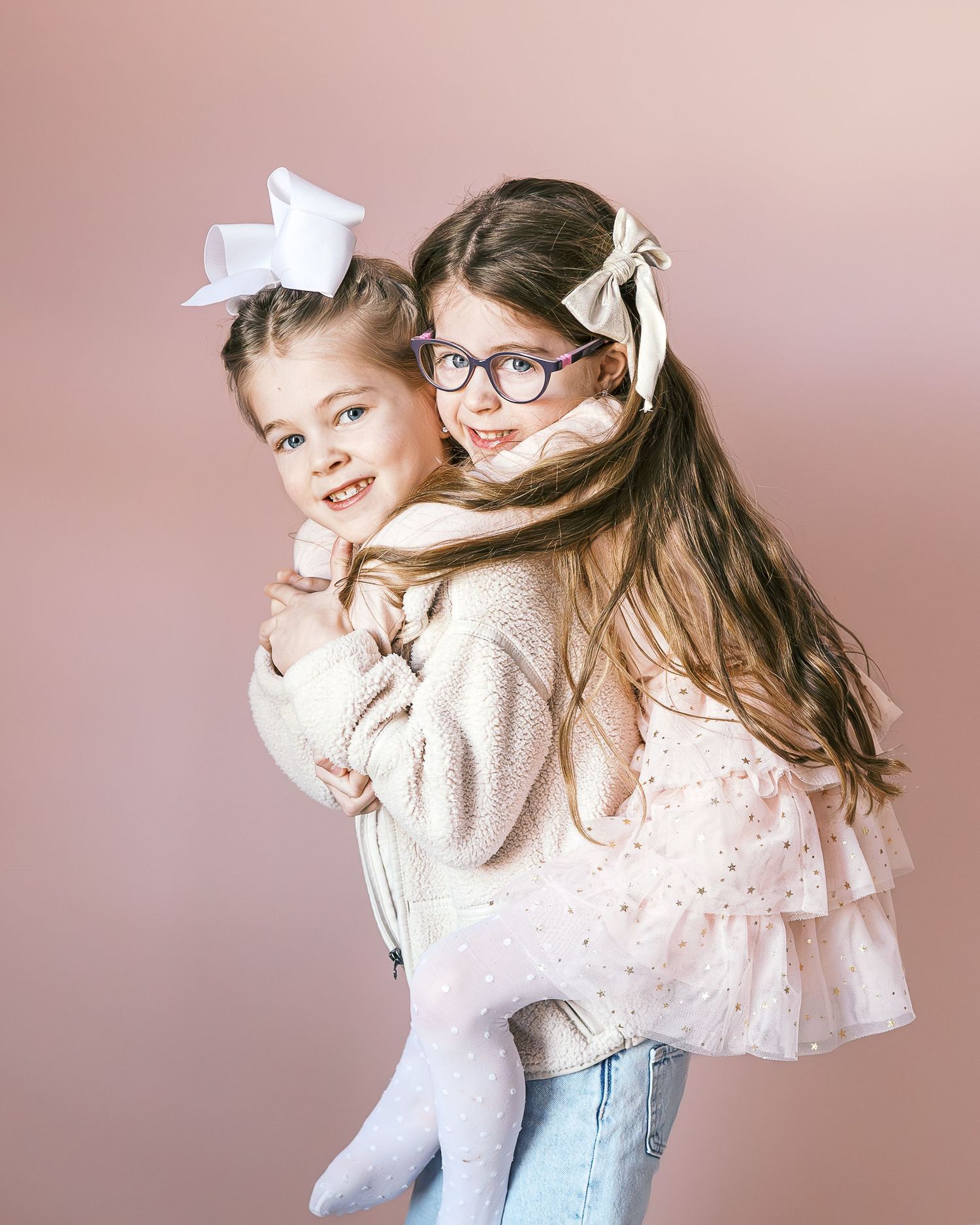 Sisters sharing joyful moments in pink room wearing casual and dressy outfits.