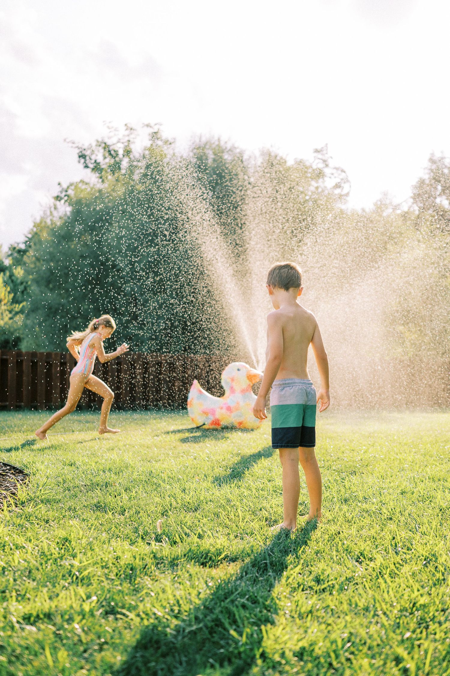 Children playing in backyard sprinklers on a bright summer day.