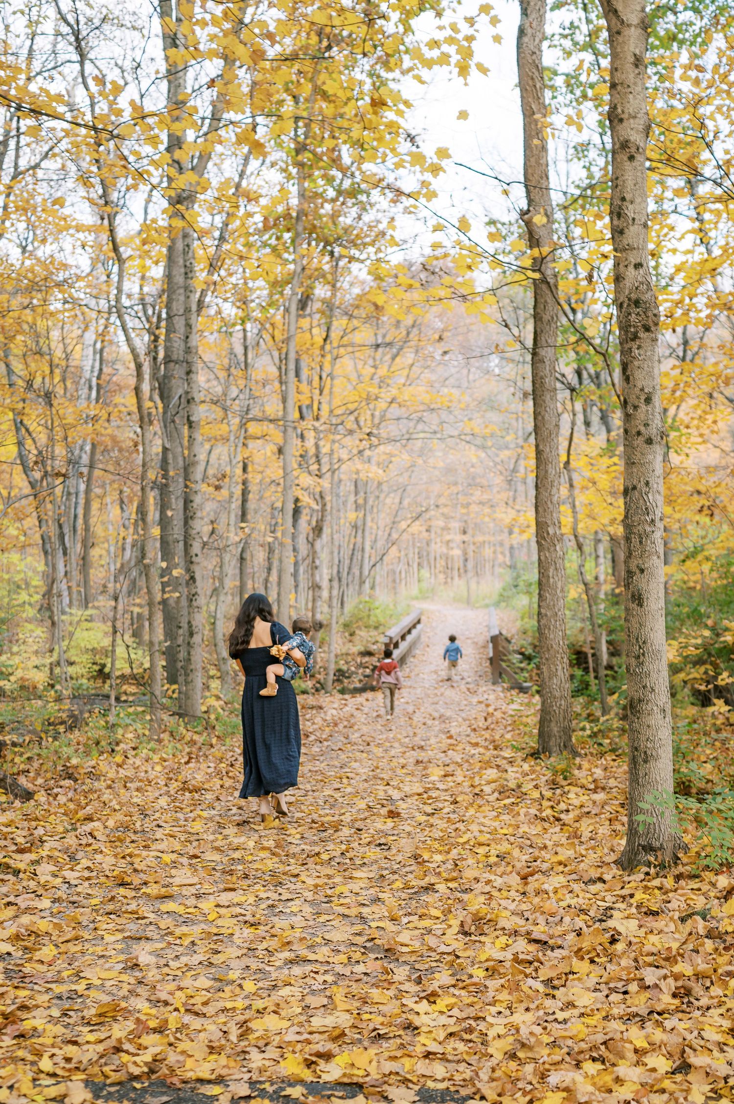 Person standing on leaf-covered path in forest with golden autumn foliage.