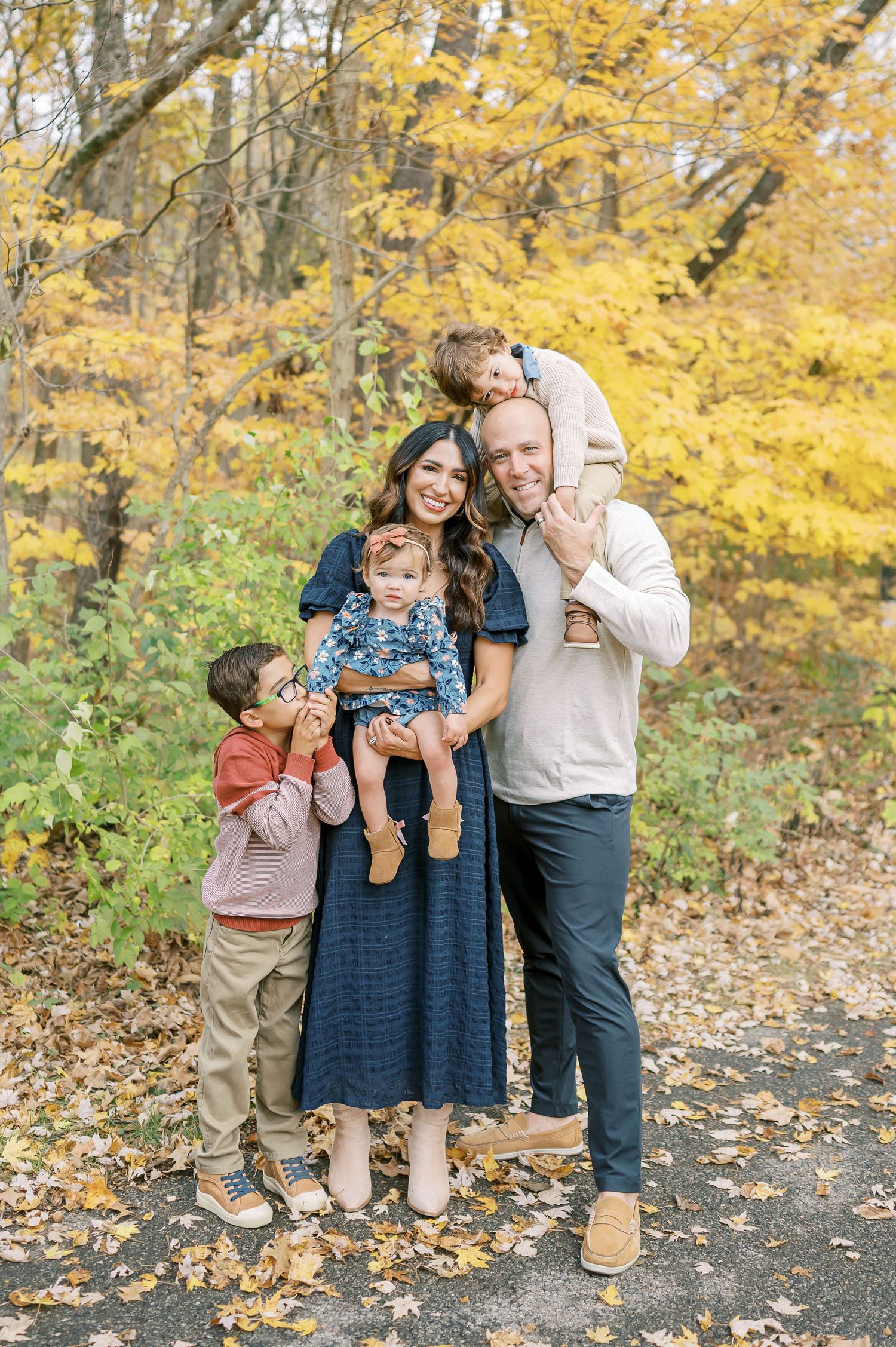 Family enjoying playful moments together on path surrounded by golden fall foliage.