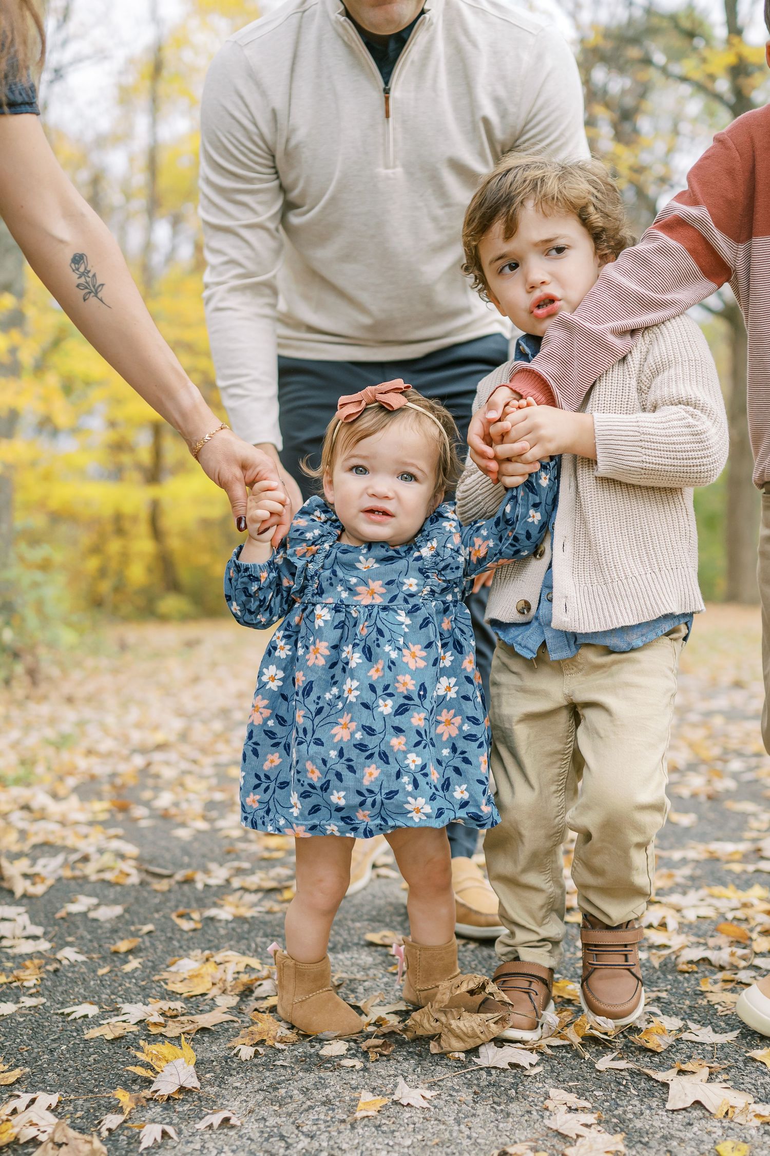 Family holding hands while walking together on leaf-covered autumn path.