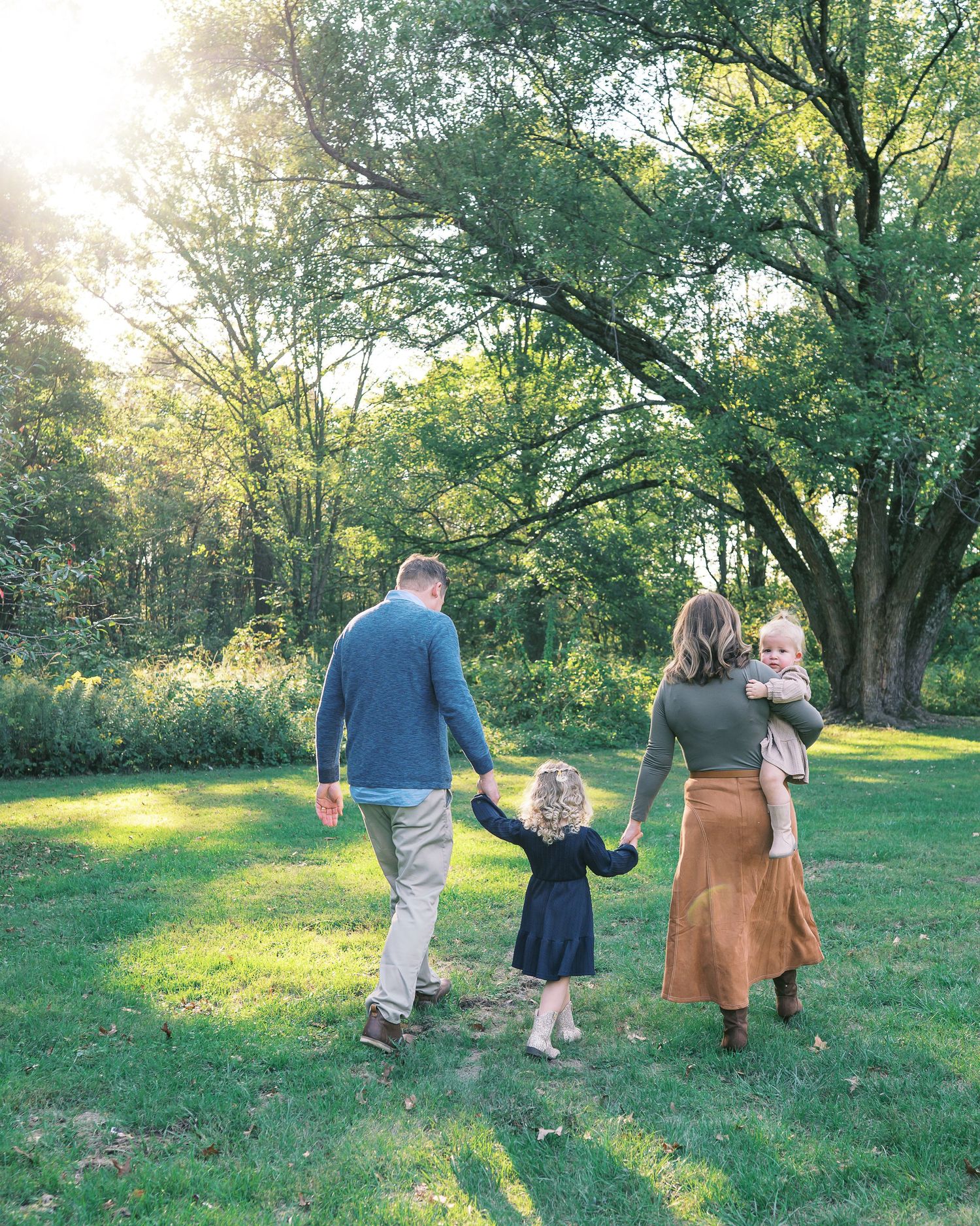 A family holds hands and walks together through a sunlit meadow on a warm afternoon.