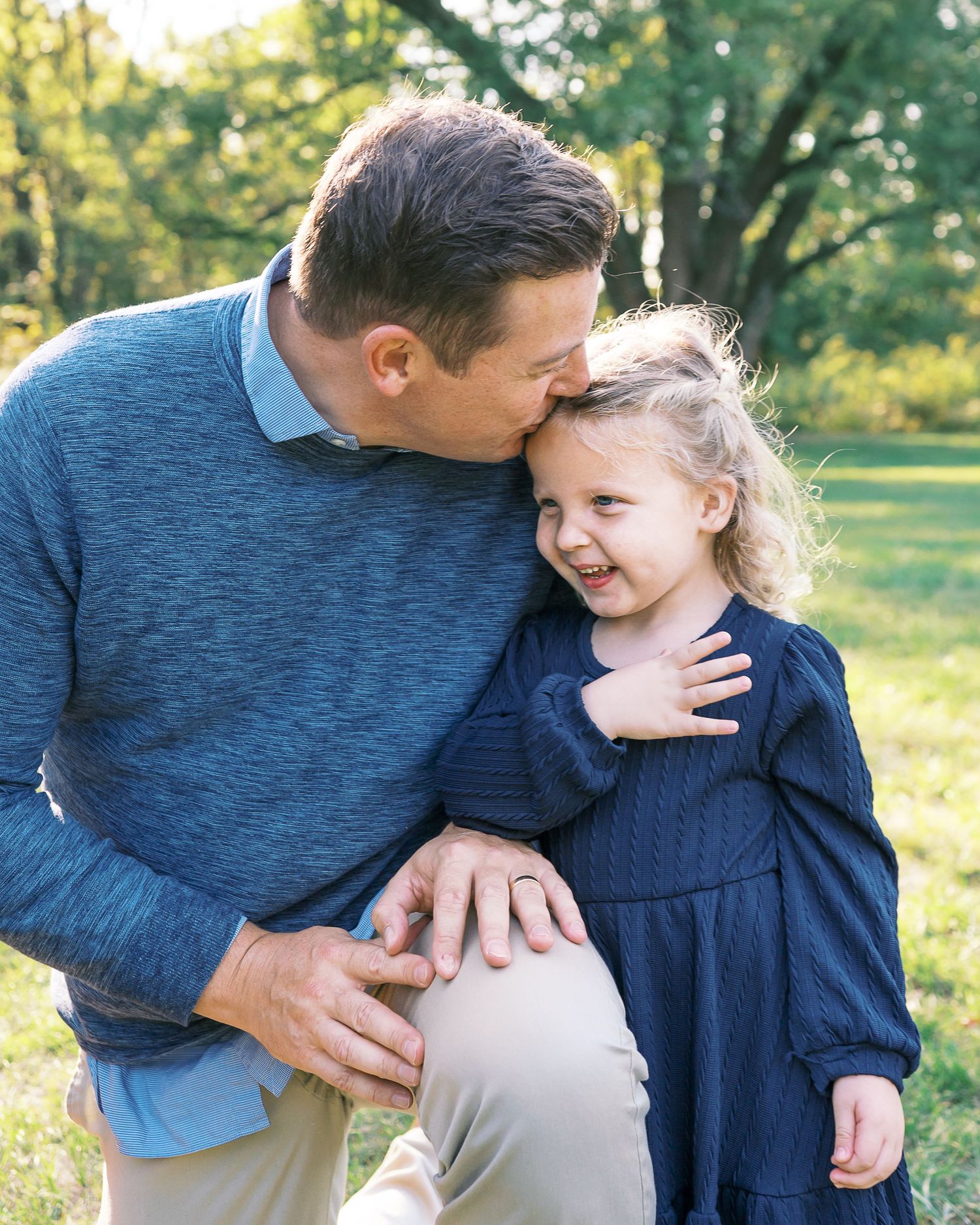 A tender moment shared between parent and child outdoors in a park with green trees in the background.