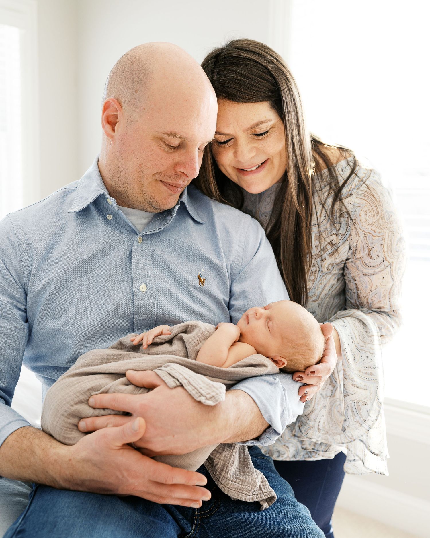 Parents lovingly cradle their newborn baby while sitting together in a bright room.